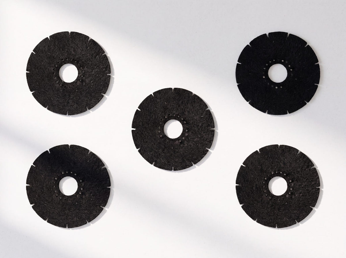 Five replacement carbon filter discs laid out on a white surface